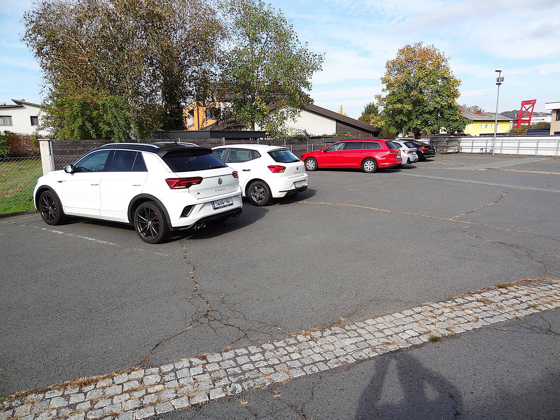 Großer asphaltierter Parkplatz mit mehreren geparkten Autos und Bäumen im Hintergrund.