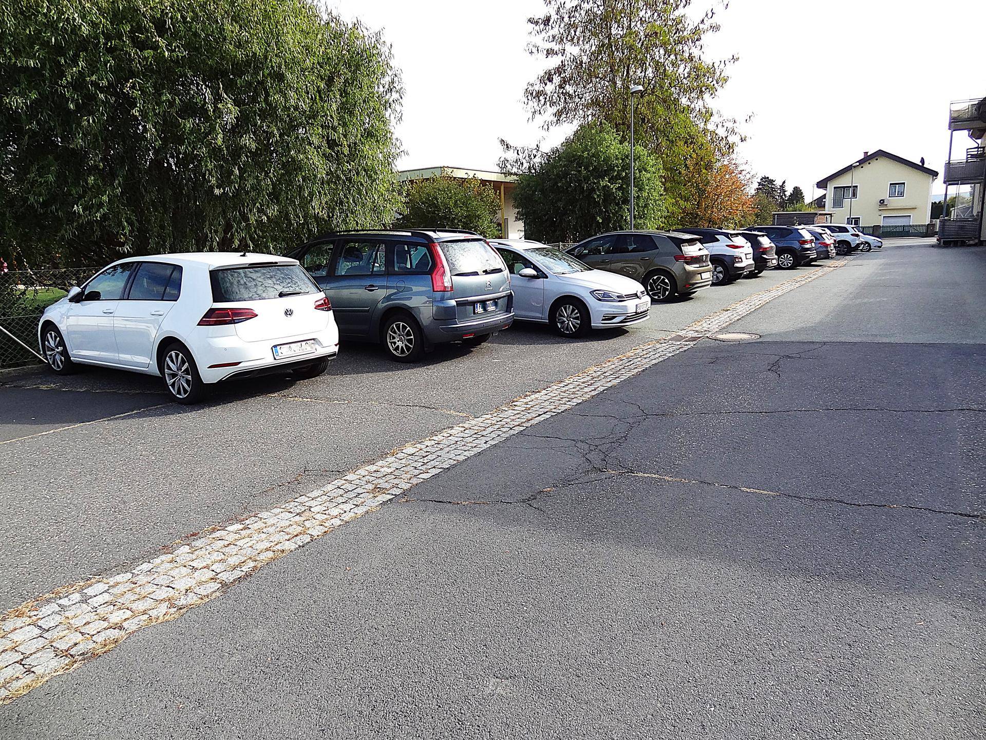 Reihe von geparkten Autos auf einem asphaltierten Parkplatz neben einer gepflasterten Kante.