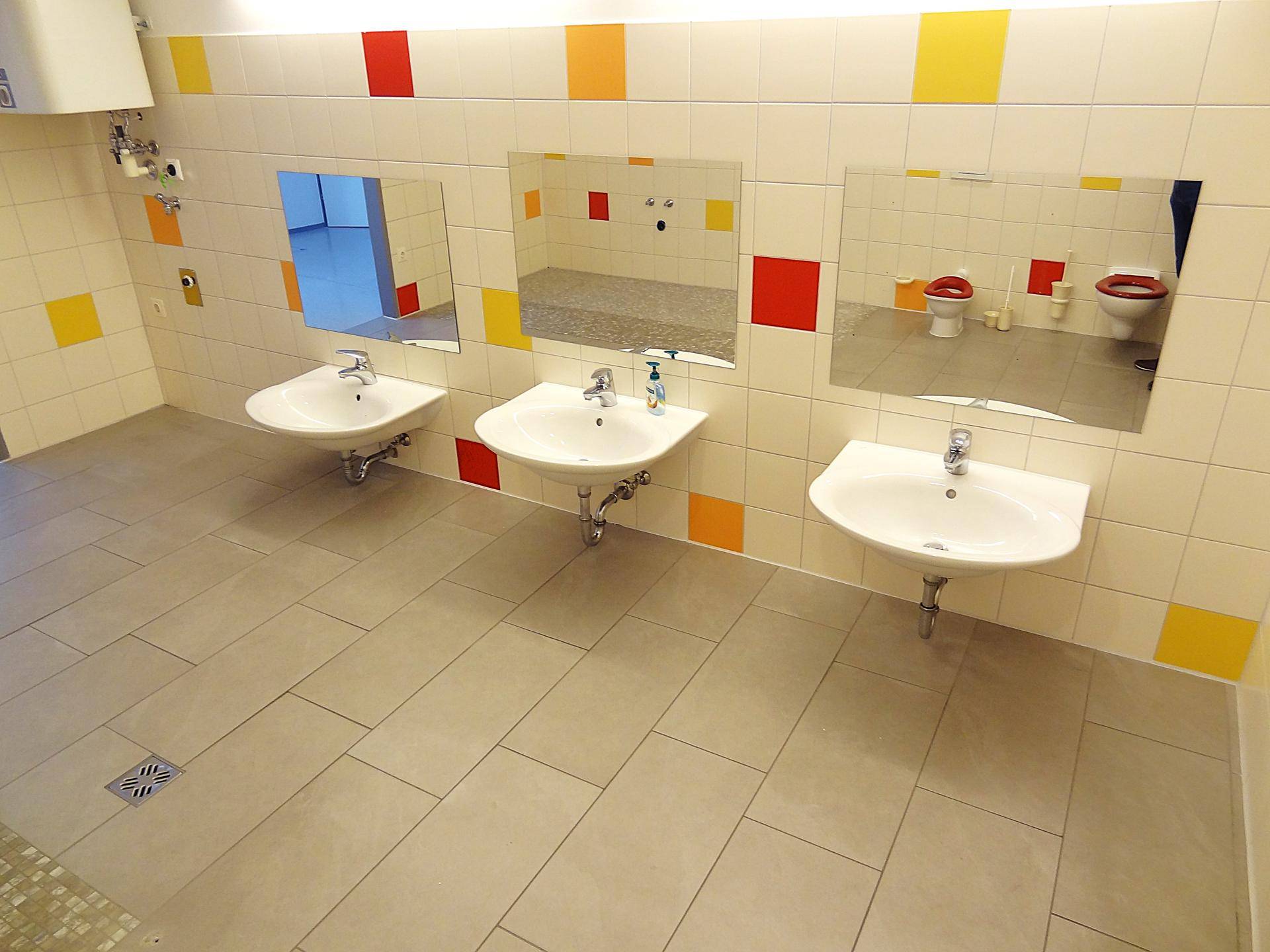 Buntes Kinderbadezimmer mit mehreren Waschbecken und Spiegeln, hell und freundlich.