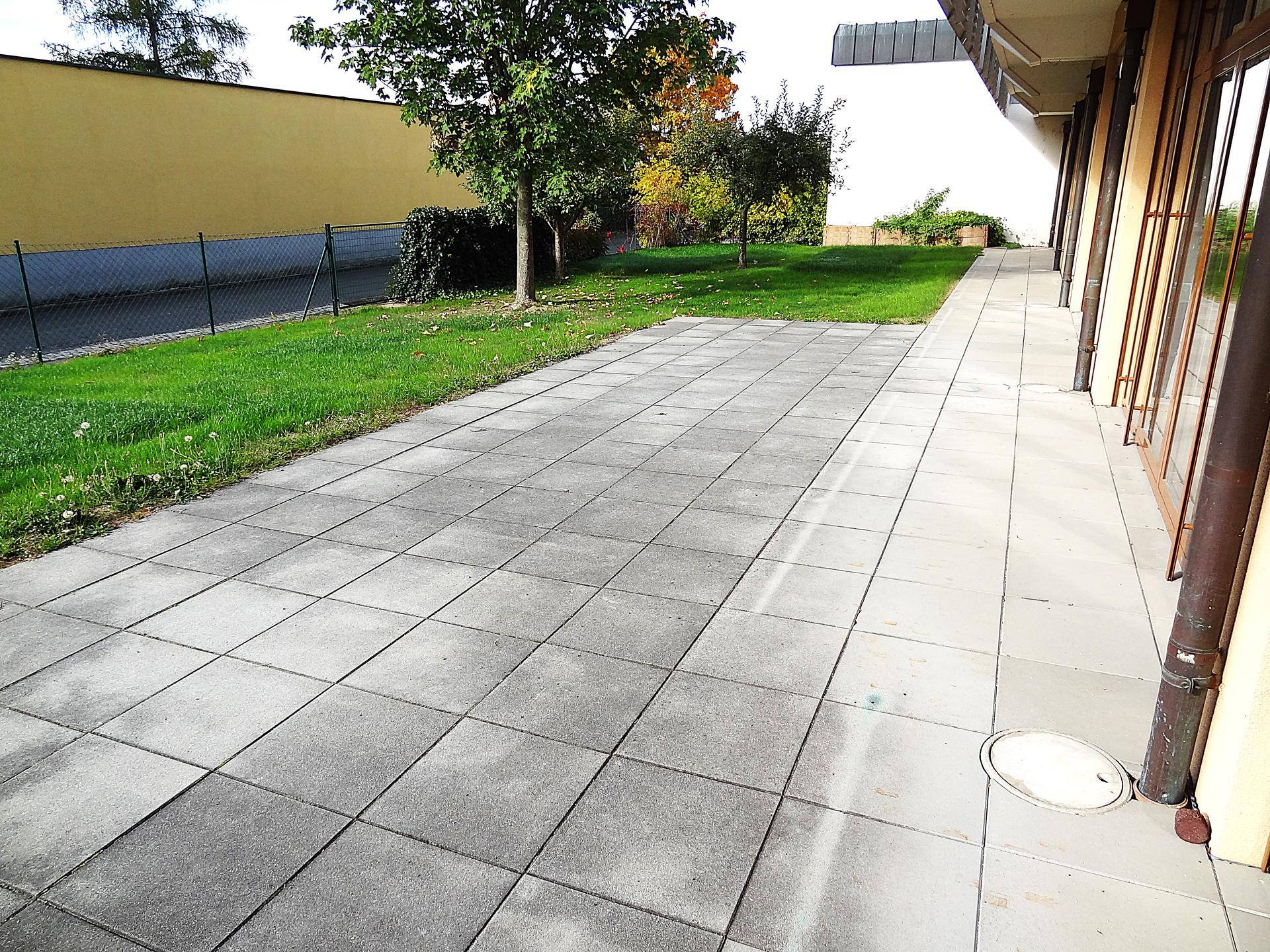 Große gepflasterte Terrasse neben einer Rasenfläche und dem Gebäude.