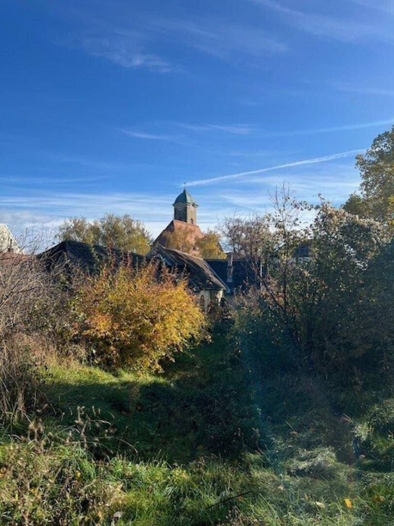 Historisches Gebäude mit Turm, umgeben von herbstlicher Vegetation unter einem klaren blauen Himmel.