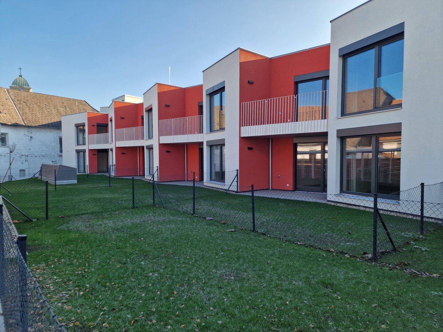 Neubauten mit zeitgenössischer Architektur, umgeben von gepflegten Grünflächen und einem Zaun.