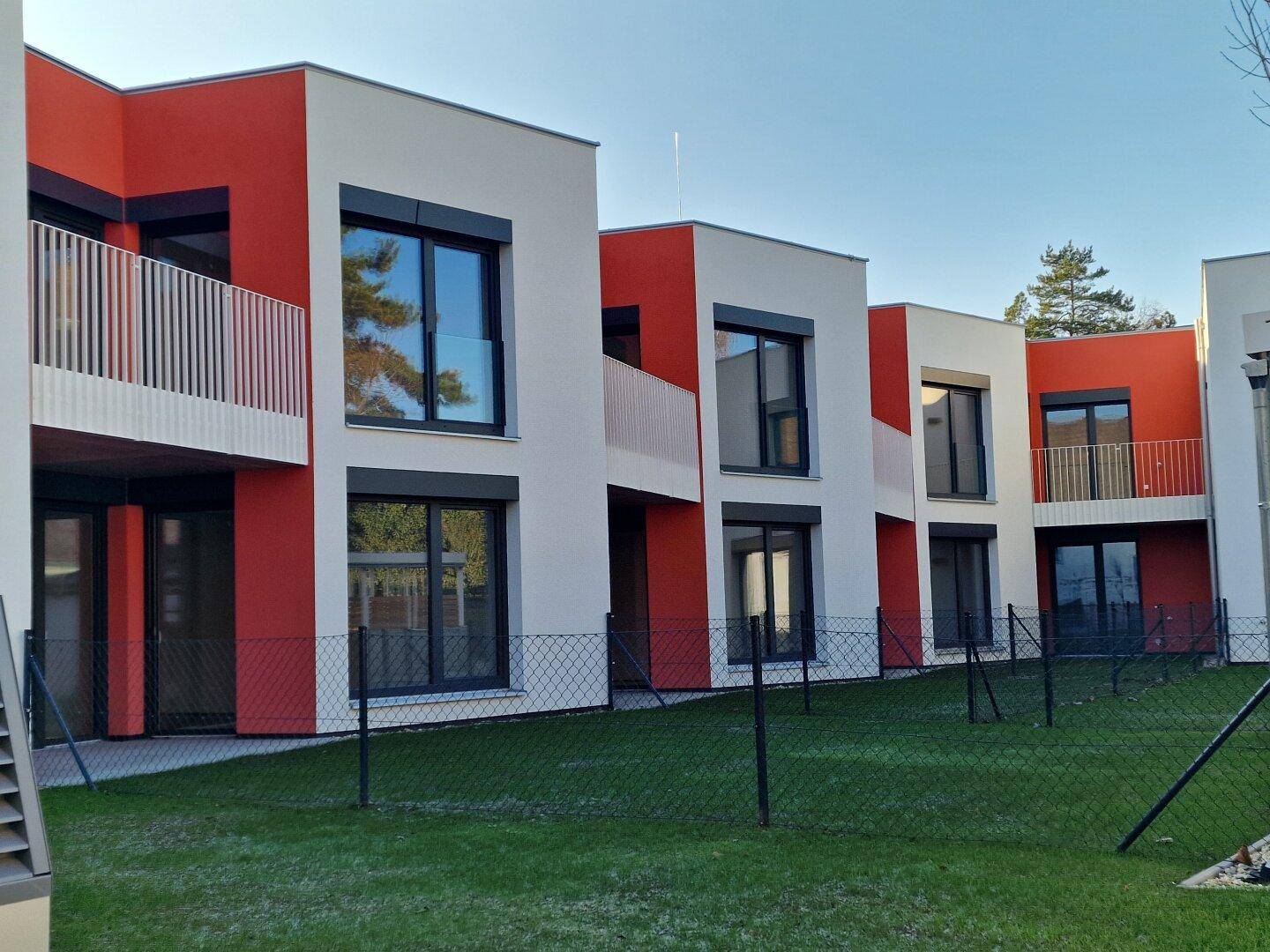 Reihe moderner Reihenhäuser mit roten und weißen Fassaden und kleinen Gärten.