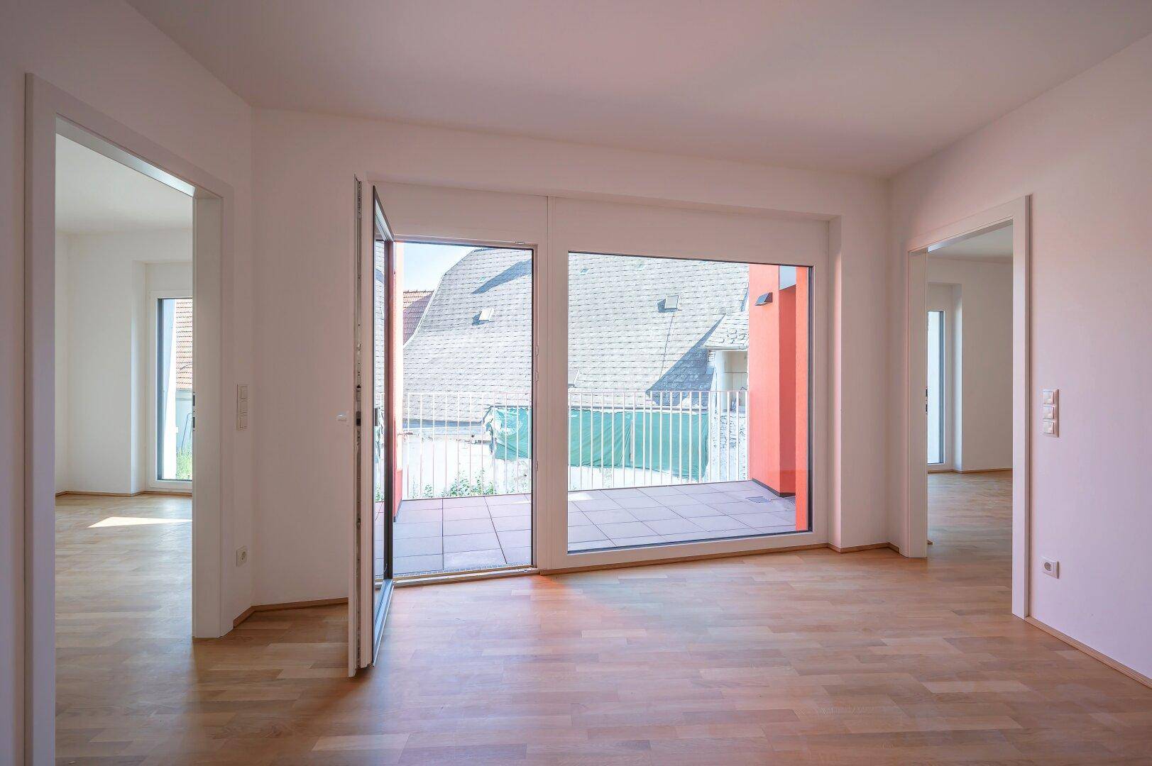 Heller Raum mit Parkettboden und direktem Zugang zur Terrasse, die einen Blick auf die Umgebung bietet.