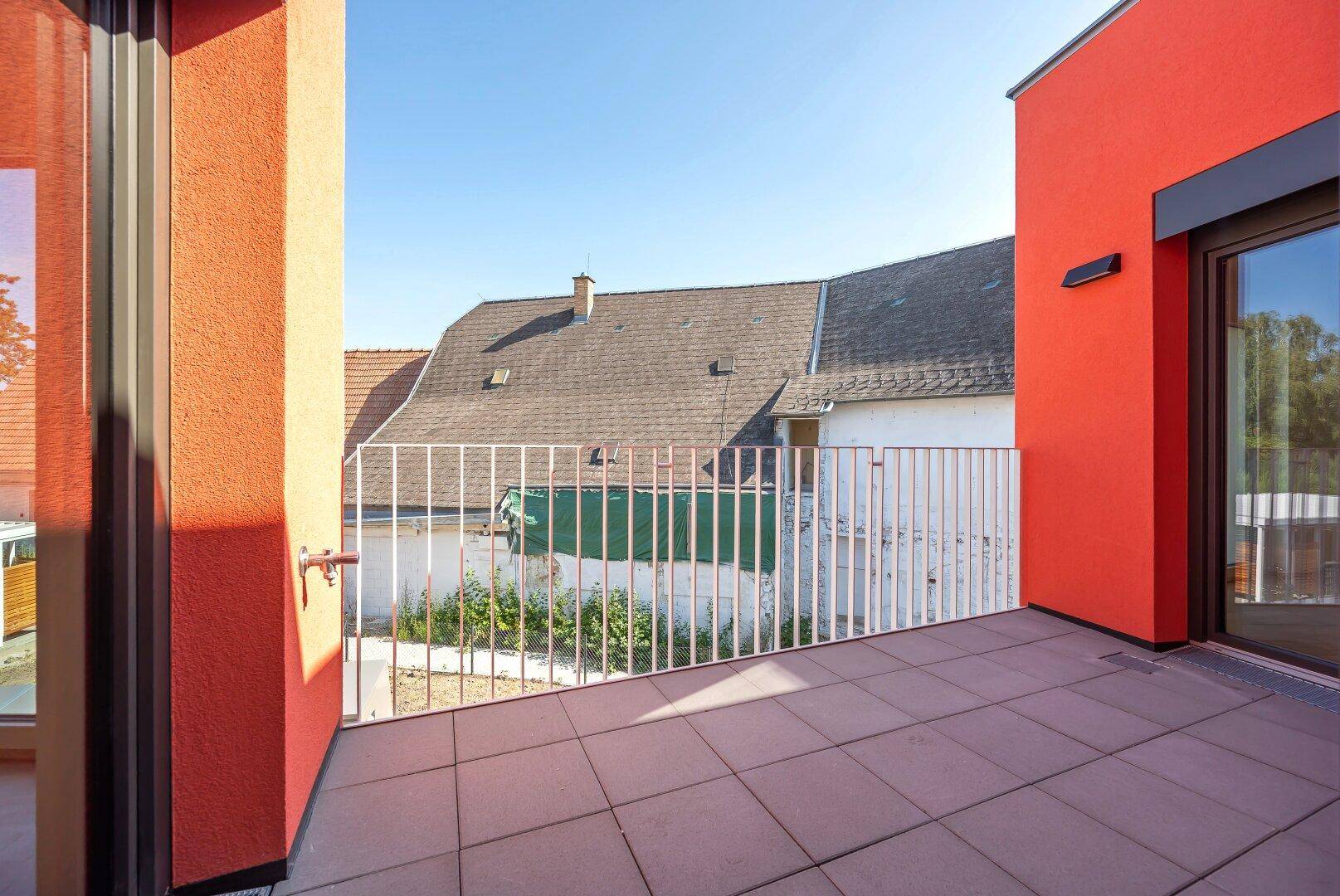 Sonniger Außenbereich mit Fliesenboden und weißem Geländer, umgeben von modernen Gebäuden.