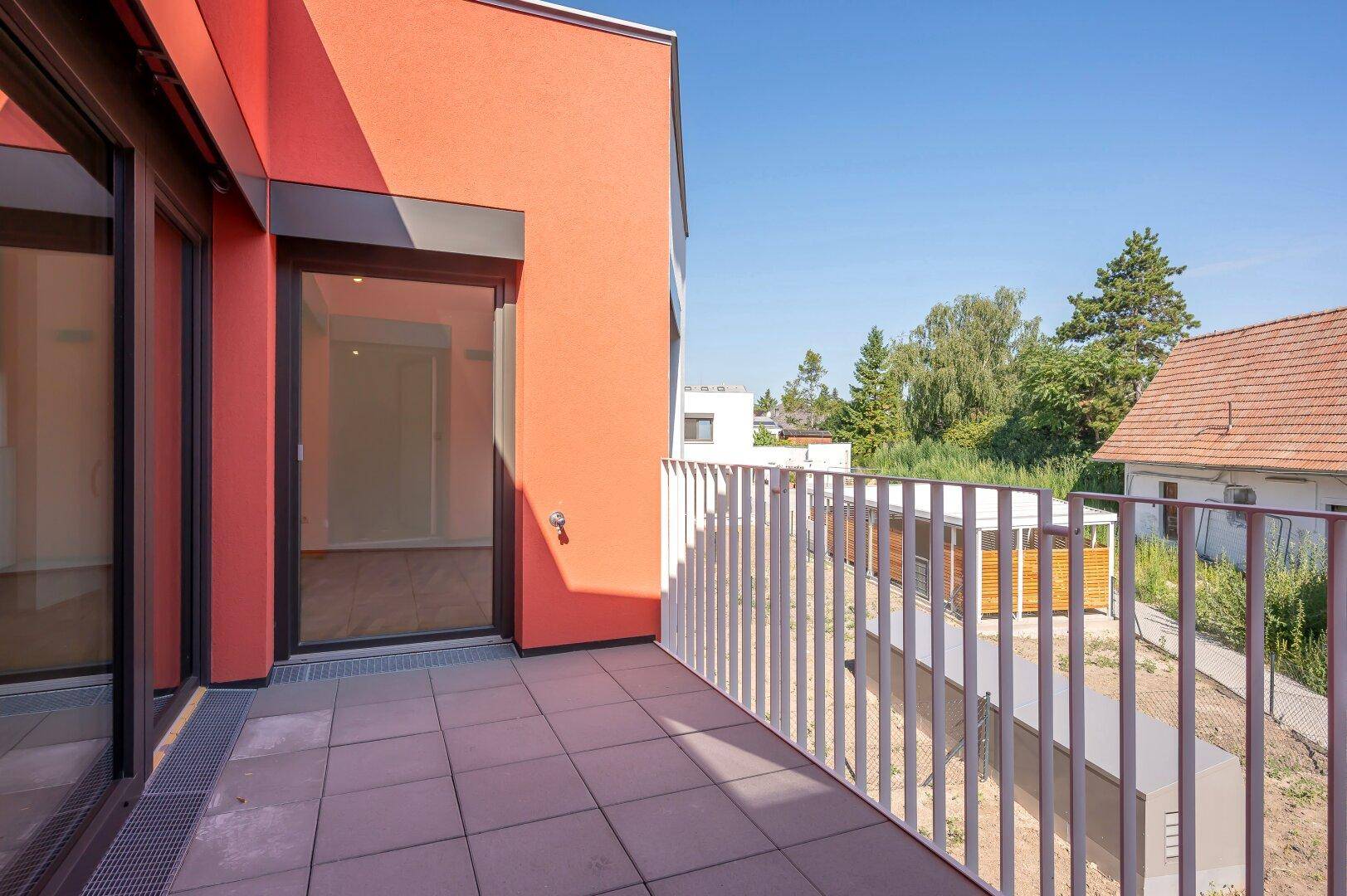 Geräumige Terrasse mit Fliesenboden und Blick auf die grüne Umgebung und weitere Gebäude.