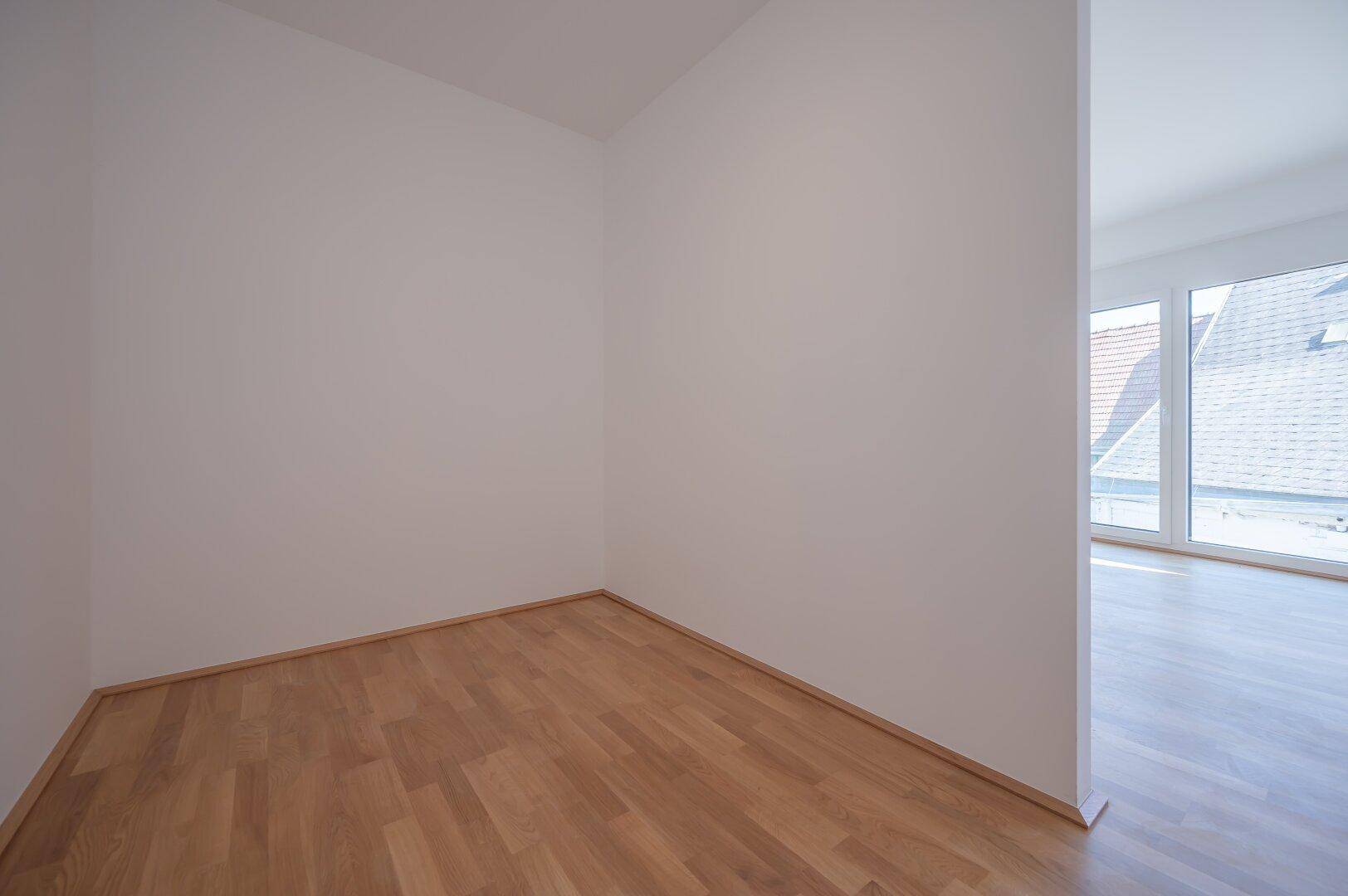 Kleiner, heller Raum mit Parkettboden und weißen Wänden, ideal als flexibler Bereich.