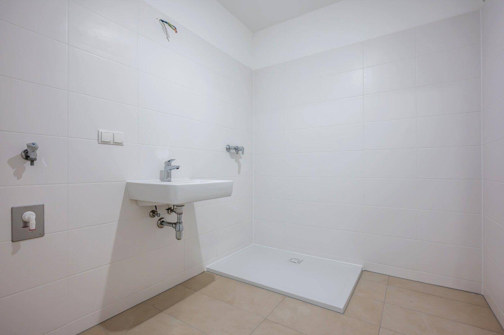 Modernes Badezimmer mit weißen Fliesen, Waschbecken und vorbereiteter Duschfläche.