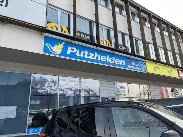 Außenansicht eines Geschäftsgebäudes mit Werbeschildern und geparkten Autos davor.