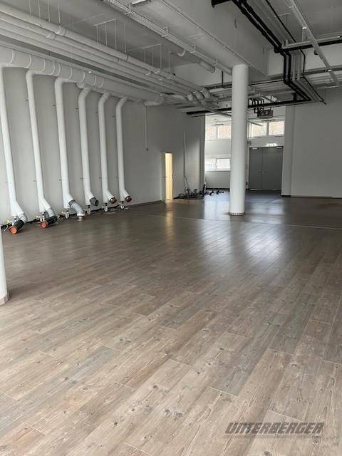 Heller und geräumiger Gewerberaum mit Säulen, sichtbaren Rohren und großen Fenstern im Hintergrund.