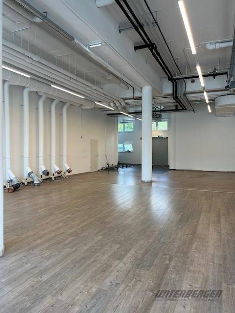 Moderner Gewerberaum mit viel Tageslicht, freiliegenden Leitungen und einem hellen Laminatboden.