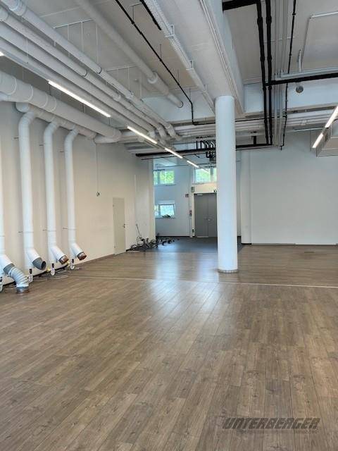 Großer, offener Gewerberaum mit sichtbaren Deckeninstallationen und modernem Laminatboden.