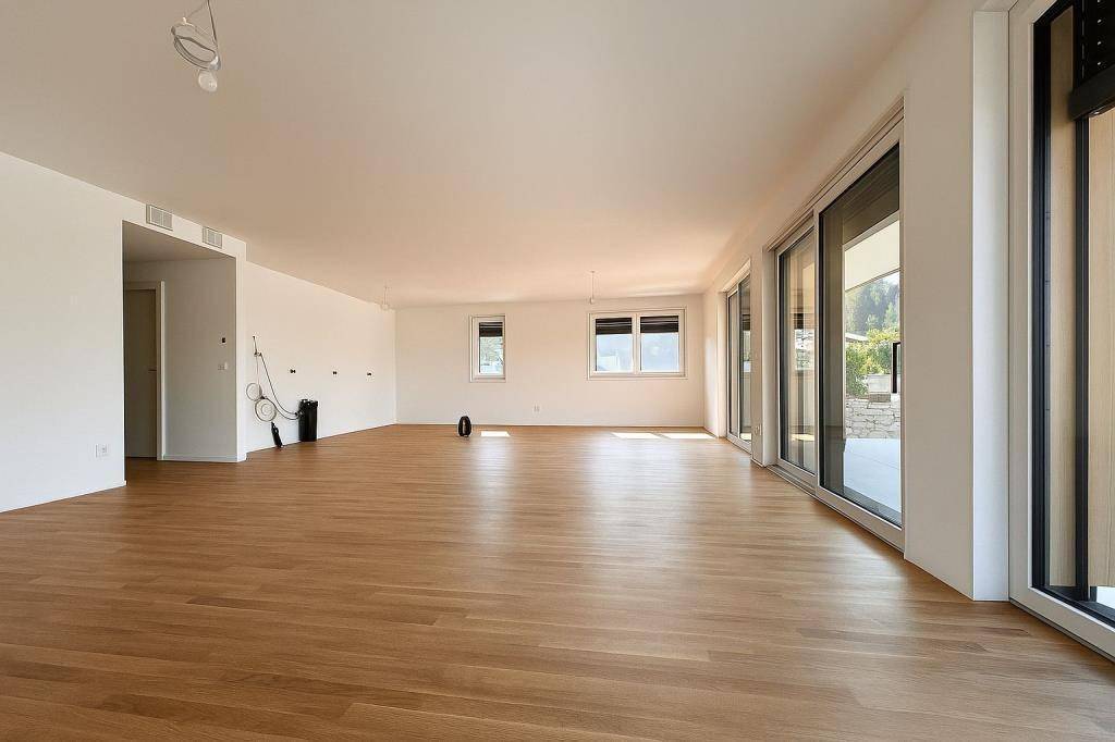 Geräumiger, unmöblierter Wohnbereich mit Holzboden und Zugang zu einer Terrasse.