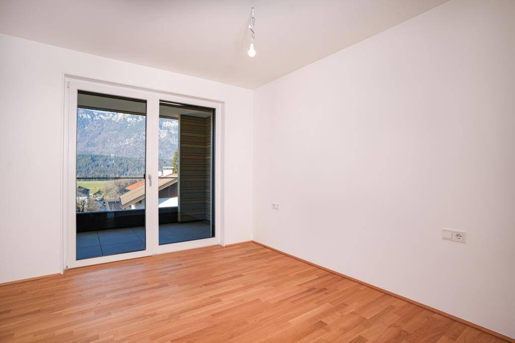 Leeres Schlafzimmer mit Parkettboden und Zugang zu einem Balkon mit Bergblick.