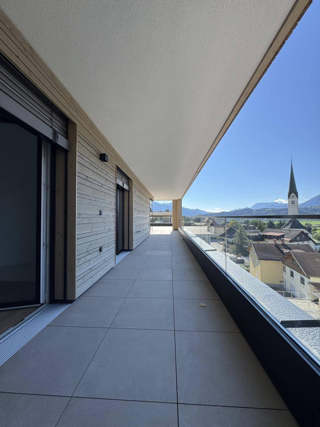 Breiter Balkon mit Glasgeländer und weitem Blick auf die Stadt und die Berge.