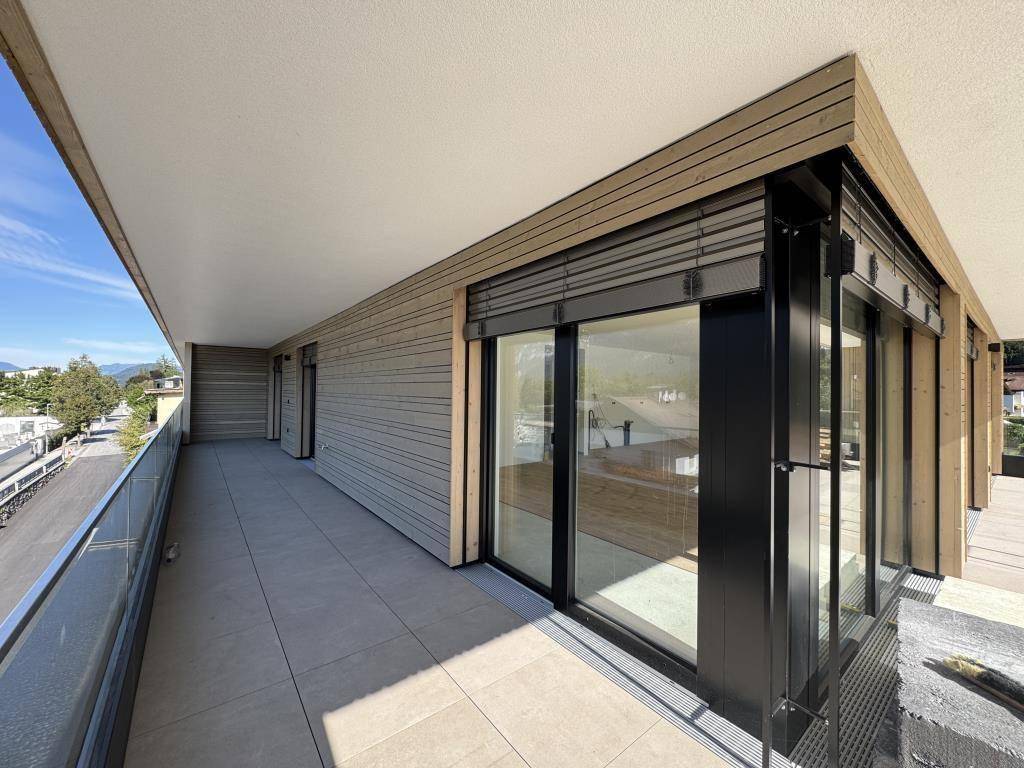 Langer, überdachter Balkon mit Fliesenboden und Holzverkleidung an der Fassade.