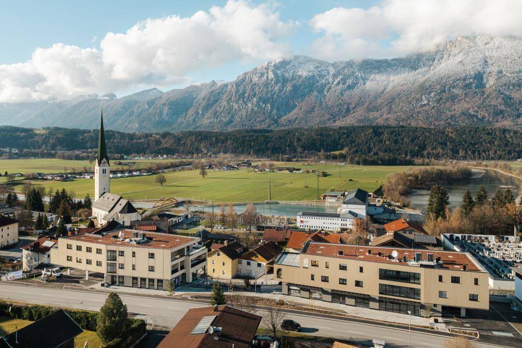Panoramablick auf eine Kleinstadt mit Kirche, Fluss und schneebedeckten Bergen im Hintergrund.