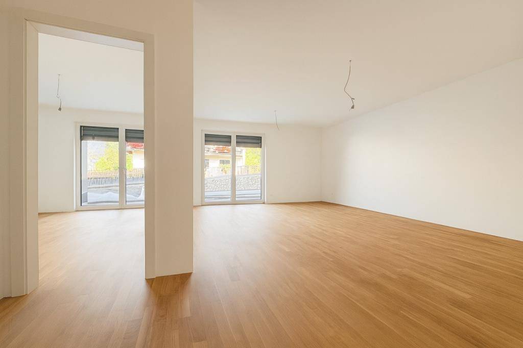 Helles, unmöbliertes Wohnzimmer mit Blick auf das daneben liegende Schlafzimmer