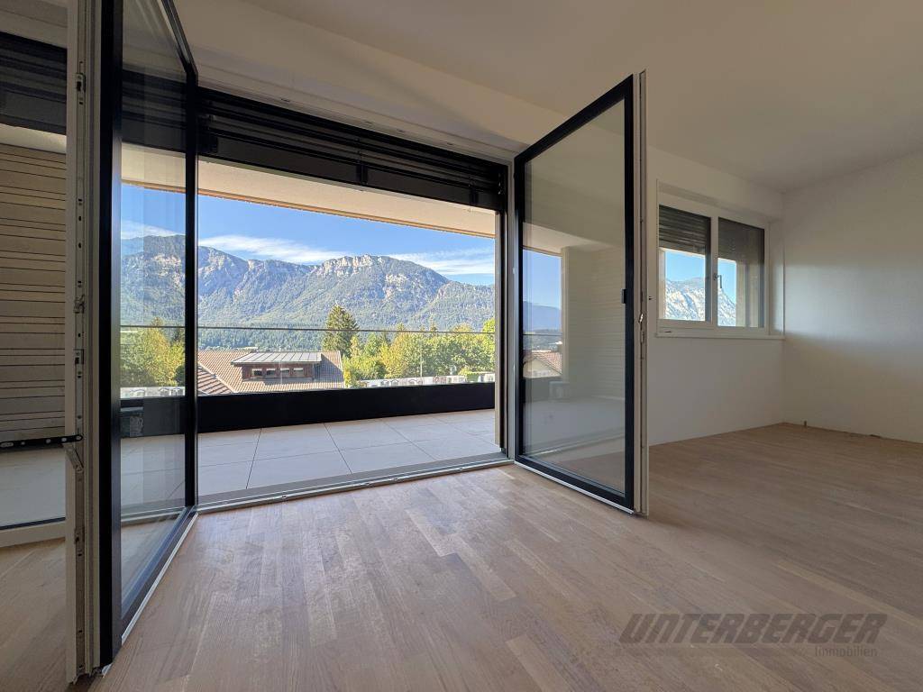 Blick aus dem Wohnzimmer durch eine offene Faltglastür auf den Balkon mit Bergpanorama
