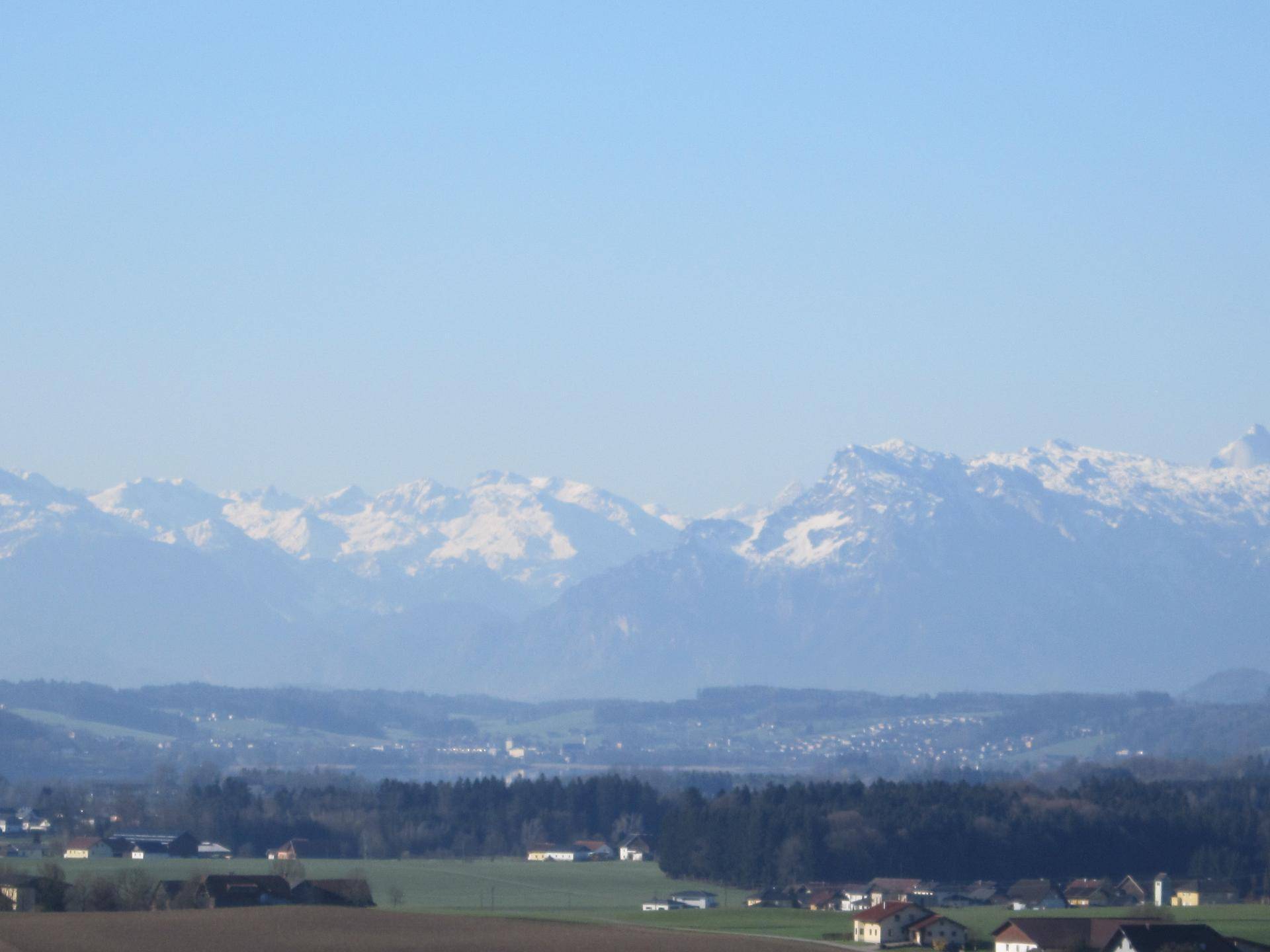 Weitläufiger Blick auf schneebedeckte Berge und die umliegende ländliche Landschaft.