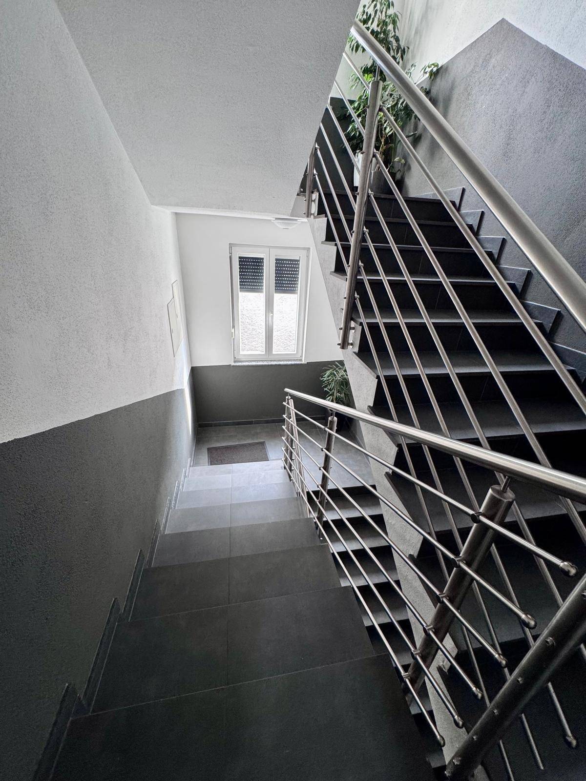 Modernes Treppenhaus mit Edelstahlgeländer und Fenster für natürliches Licht.