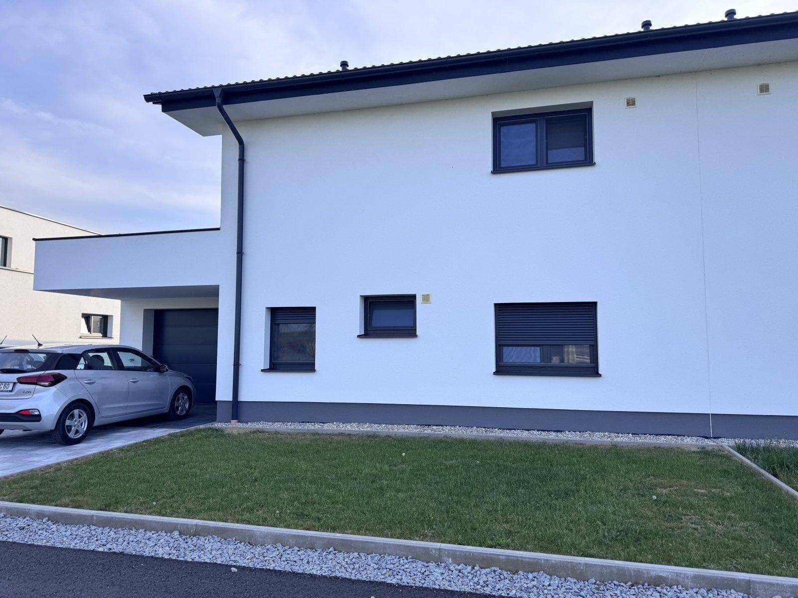 Moderne Hausfassade in Weiß mit dunklen Fenstern und Garagenzufahrt.