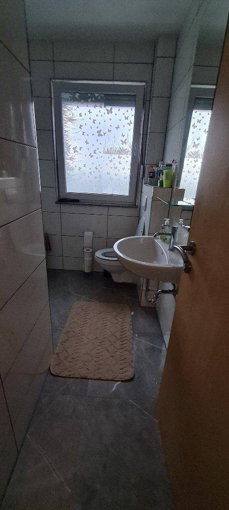 Kleines Badezimmer mit WC, Waschbecken und Fenster, gefliest in hellen Tönen.