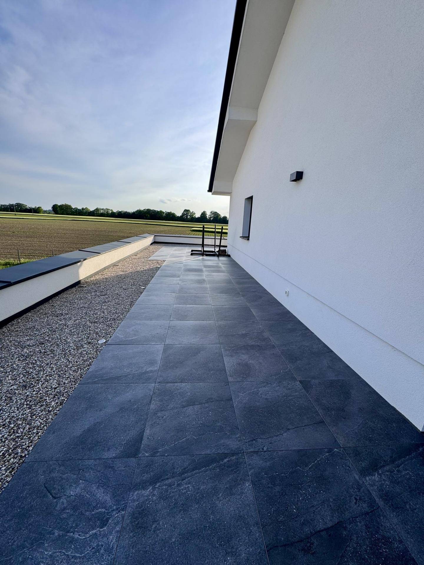 Weitläufige Terrasse mit dunklen Fliesen und freiem Blick auf die Felder.