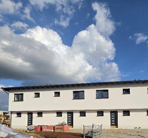 Fassade einer Reihe von Neubauten mit weißem Putz und dunklen Fenstern unter einem blauen Himmel.