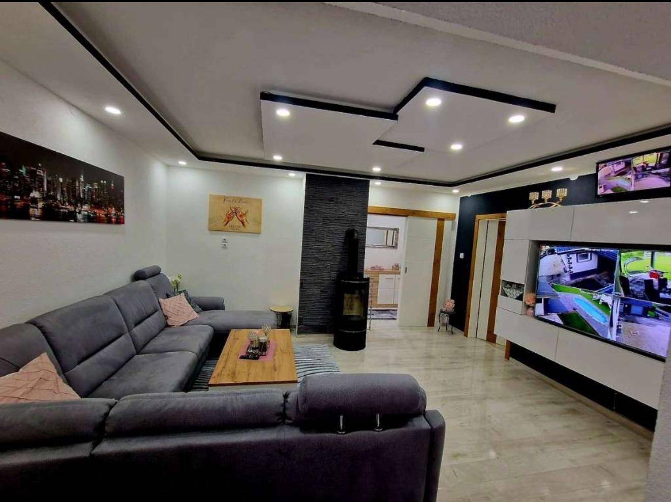 Geräumiges Wohnzimmer mit großem Sofa, Fernseher und modernem Kaminofen.