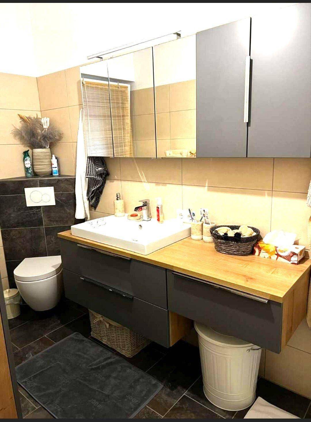 Modernes Badezimmer mit Waschtisch, Spiegel und Wand-WC, ausgestattet mit dunklen und hellen Fliesen.