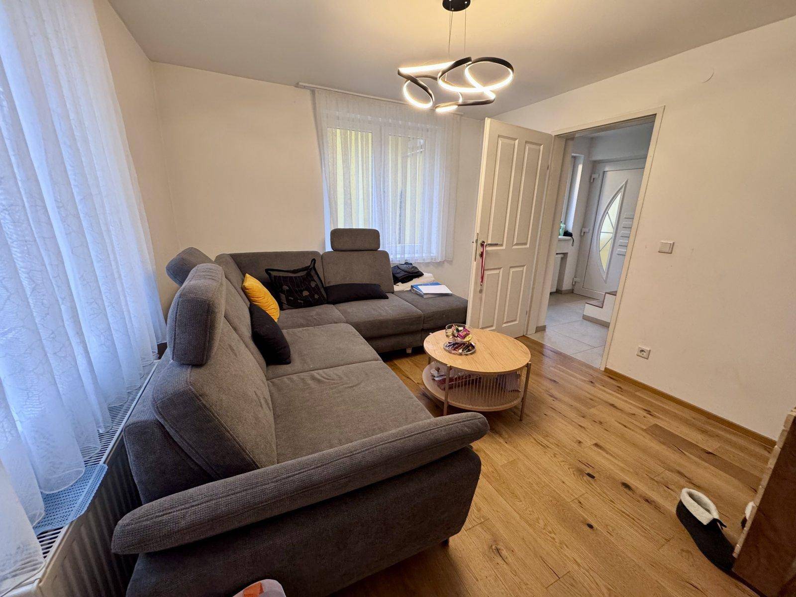 Heller Wohnbereich mit bequemem Ecksofa, Holzboden und Zugang zu einem weiteren Raum.