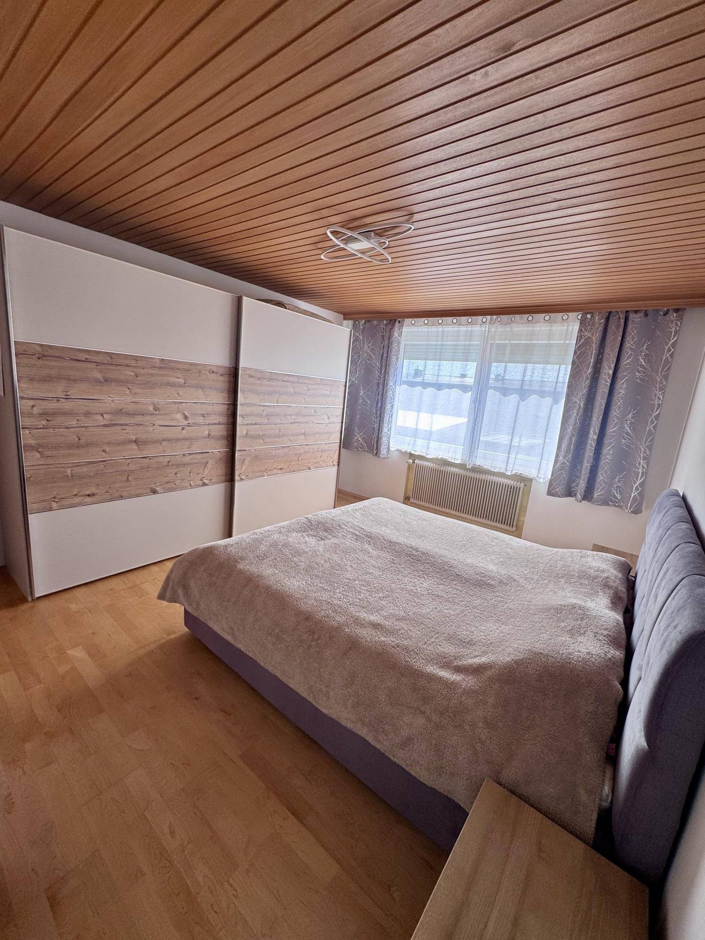 Geräumiges Schlafzimmer mit Doppelbett, Schiebetürenschrank, Holzboden und Holzdecke.