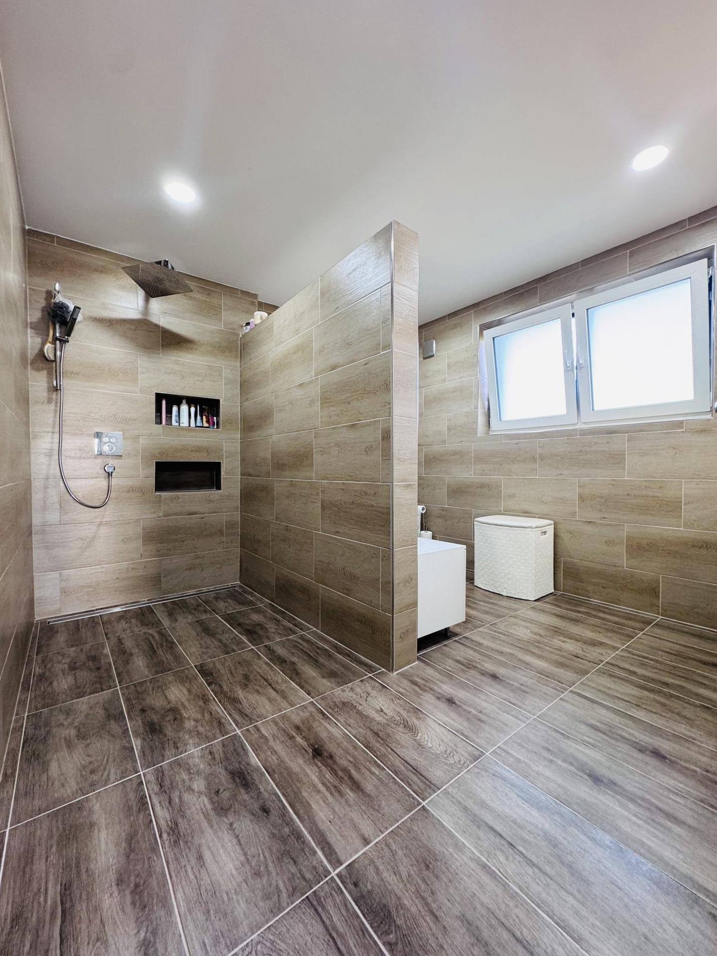 Modernes Badezimmer mit großer begehbarer Dusche, Holzoptik-Fliesen und Fenster.