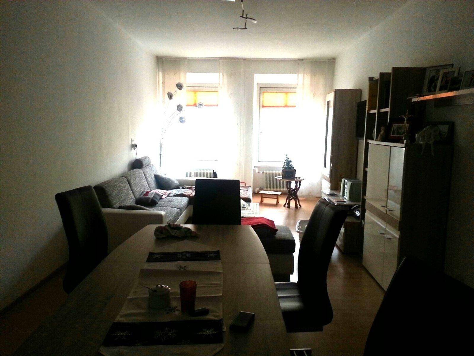 Wohn- und Essbereich mit Holzboden, Sofa und Esstisch, hell durch große Fenster.