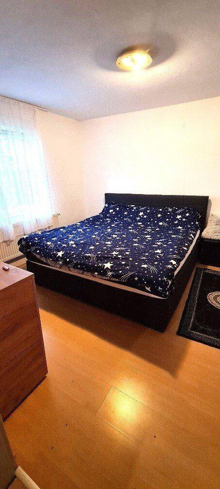 Helles Schlafzimmer mit Doppelbett, Parkettboden und weißen Wänden, schlicht gestaltet.