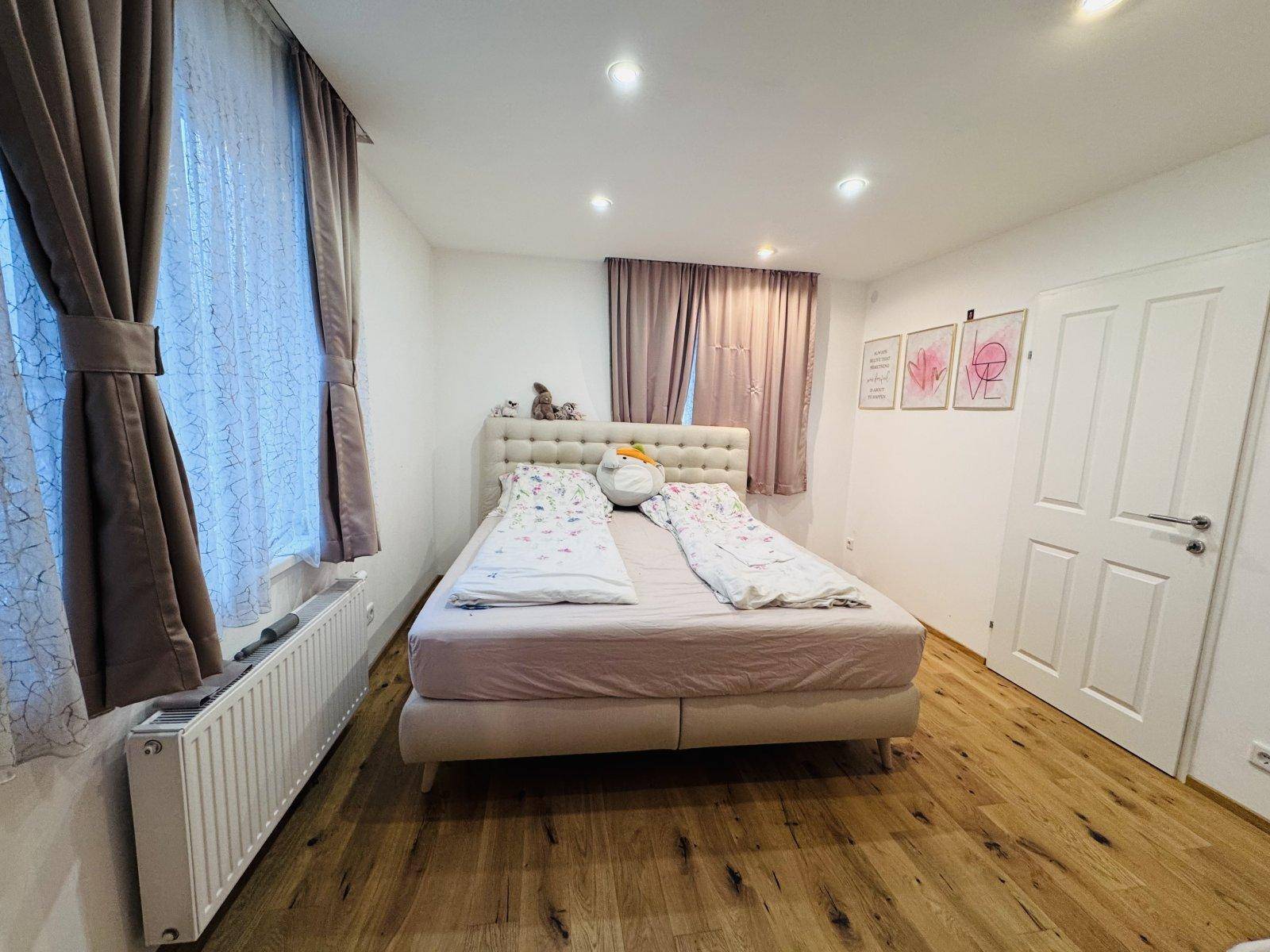 Gemütliches Schlafzimmer mit Doppelbett, Holzboden und Vorhängen an den Fenstern.