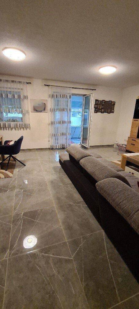 Geräumiges Wohnzimmer mit dunklen Fliesen, großem Sofa und Zugang zum Außenbereich.