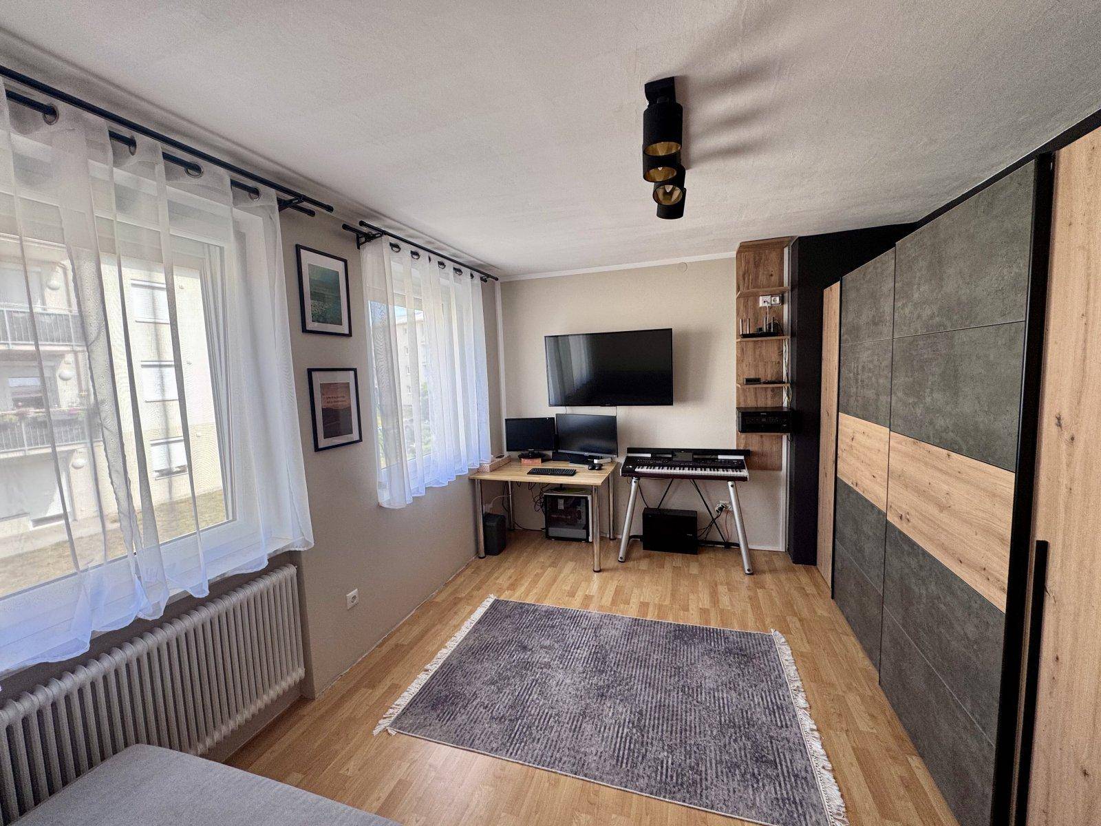 Schlafzimmer oder Arbeitszimmer mit Holzboden, Schreibtisch, Fernseher und großem Kleiderschrank.