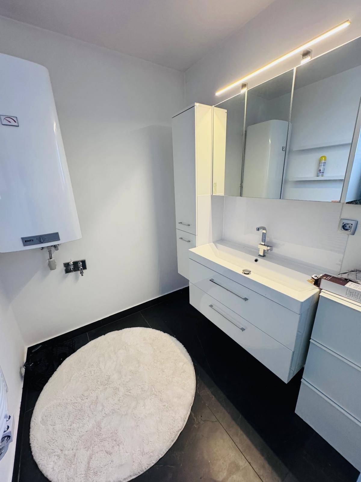 Modernes Badezimmer mit Waschtisch, Spiegelschrank und Warmwasserboiler.