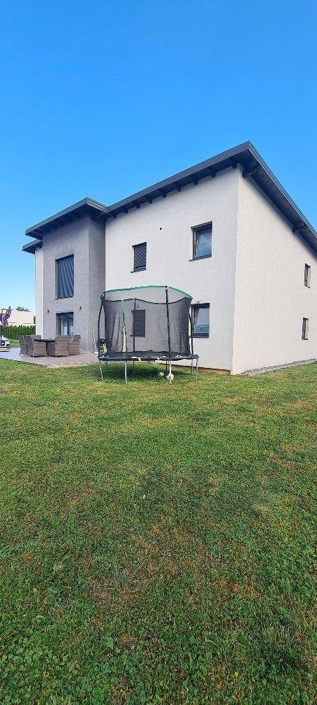 Rückseite des modernen Hauses mit großem Rasenbereich und Trampolin im Garten.