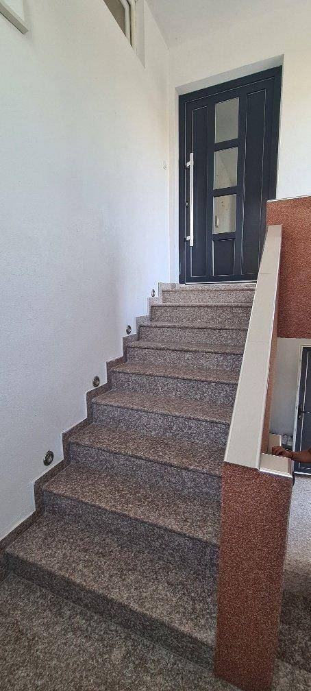 Oberer Bereich des Treppenhauses mit Granitstufen und einer modernen Eingangstür.
