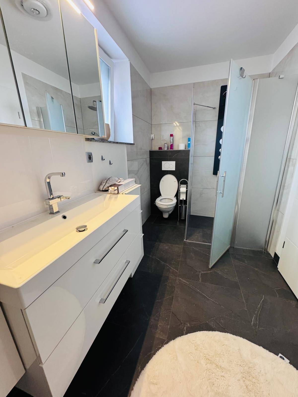 Zeitgemäßes Badezimmer mit Waschtisch, Toilette und Duschkabine, hell gefliest.