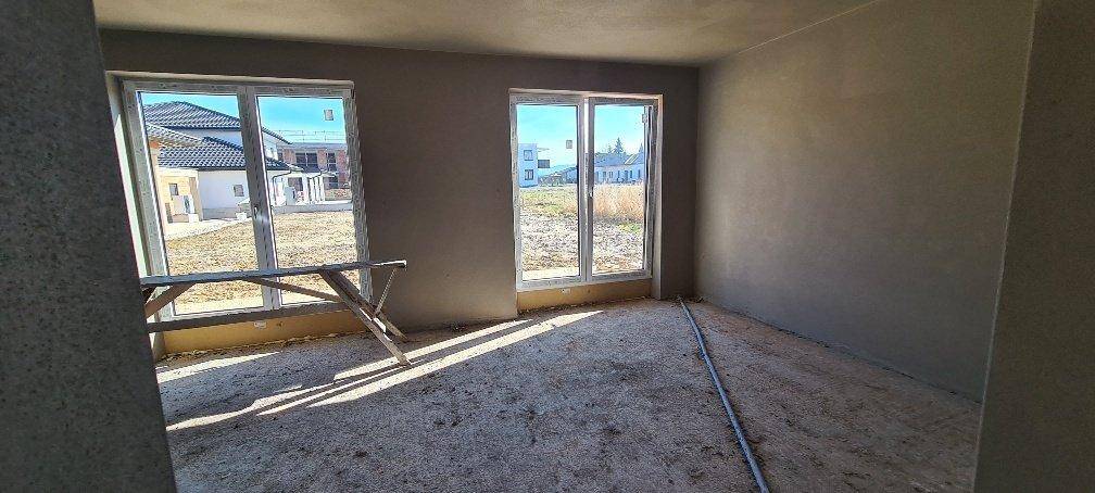 Unfertiger Innenraum mit großen Fenstern, die viel Tageslicht hereinlassen und Blick auf die Umgebung bieten.