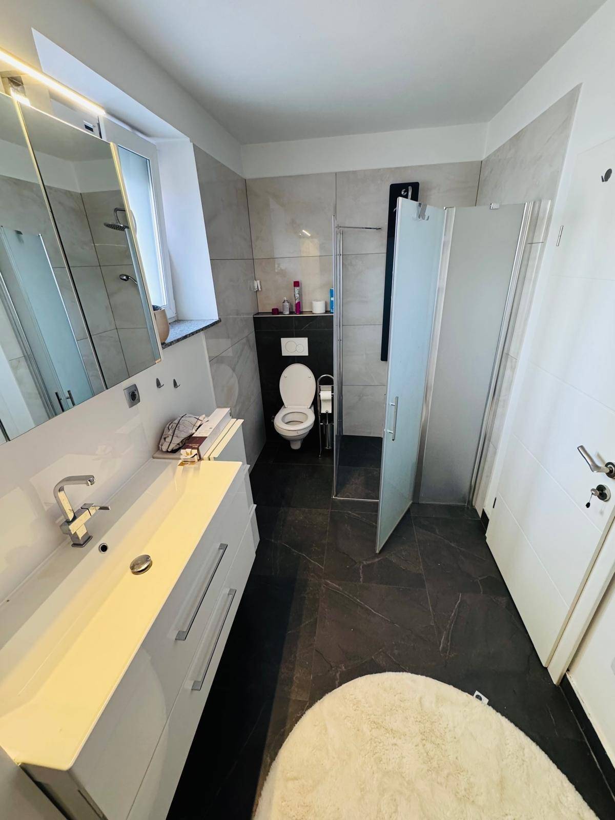 Zeitgemäßes Badezimmer mit Waschtisch, Toilette und Duschkabine, hell gefliest.