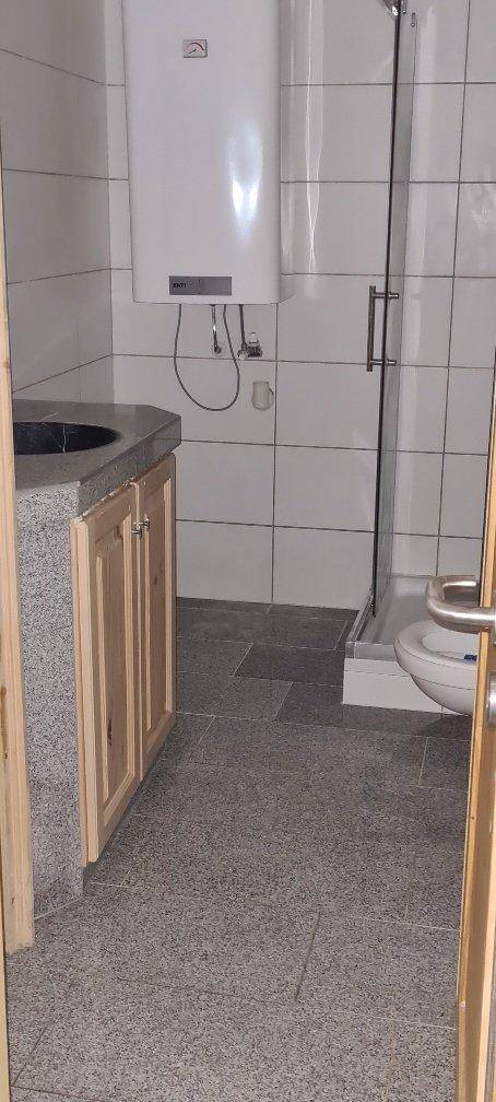 Funktionales Badezimmer mit Duschkabine, WC, Waschbecken und Warmwasserboiler an der Wand.