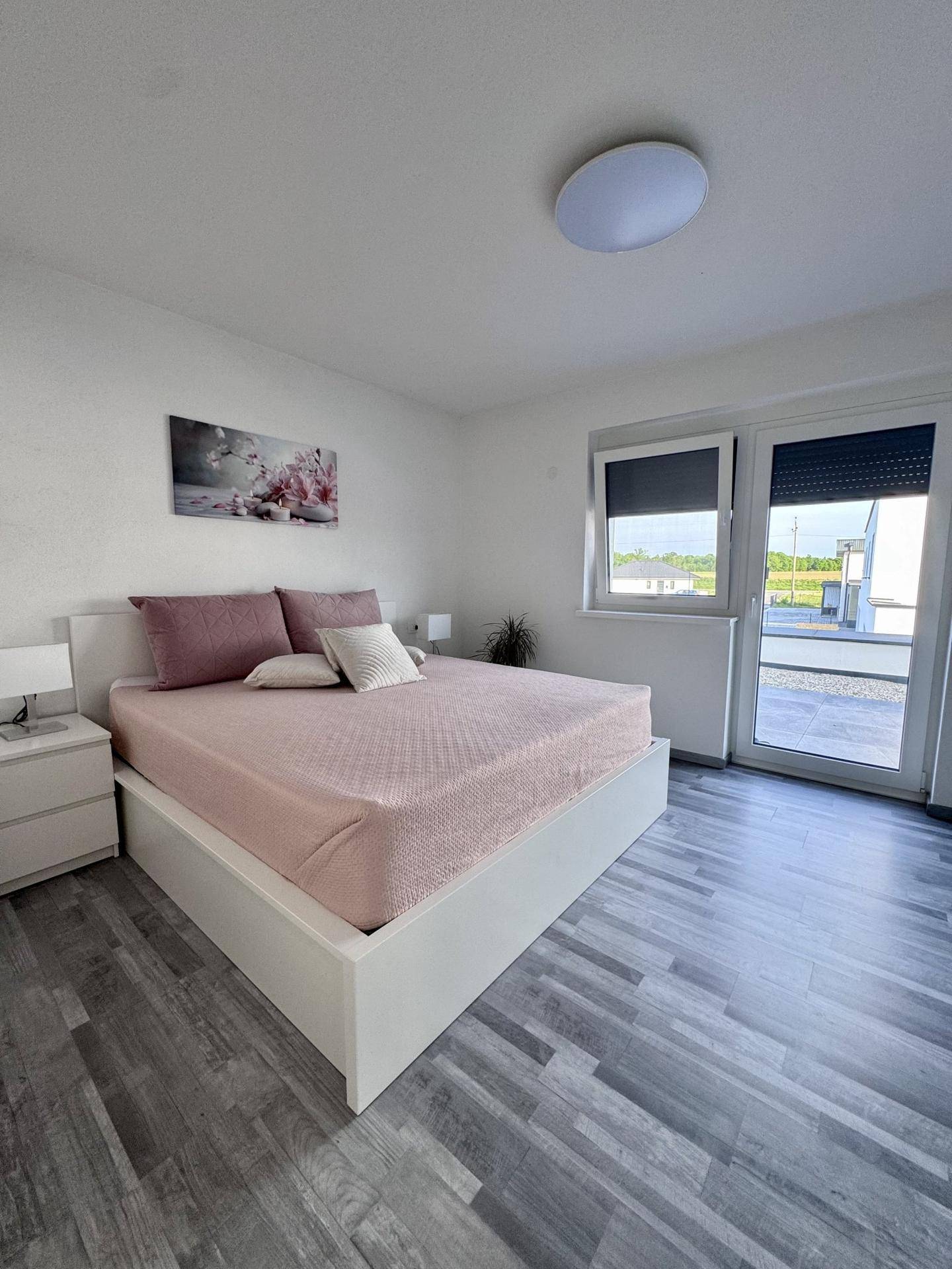 Helles Schlafzimmer mit Doppelbett, Laminatboden und Zugang zu einem Außenbereich.