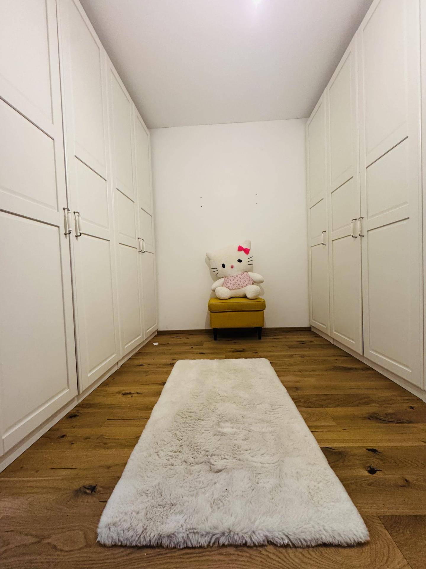 Geräumiger begehbarer Kleiderschrank mit weißen Einbauschränken und Holzboden.
