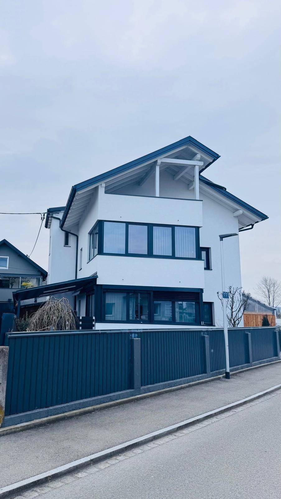 Vertikale Ansicht der modernen Hausfassade mit Balkon und großen Fensterfronten.
