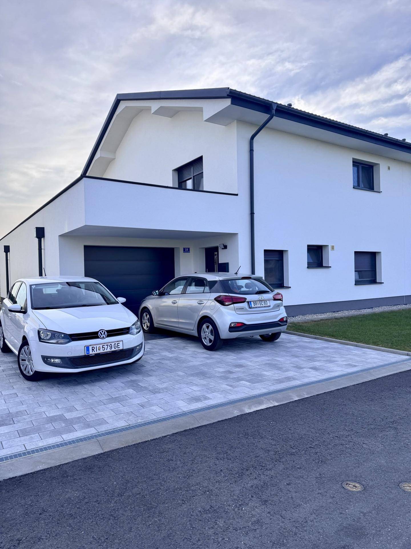 Modernes Einfamilienhaus mit gepflasterter Einfahrt und zwei parkenden Autos.